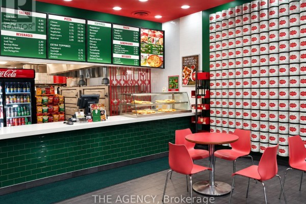 Interior of a pizza restaurant with a service counter, menu boards, pizza display, and red chairs around a small table. - 6050 Highway 7 E, Markham