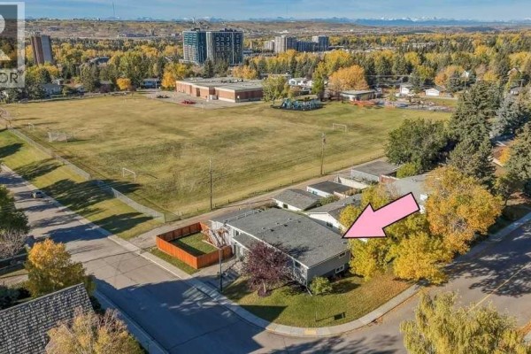 Aerial view of a house with a large grassy field and buildings in the background. - 6051 Dalgetty Drive Nw, Calgary