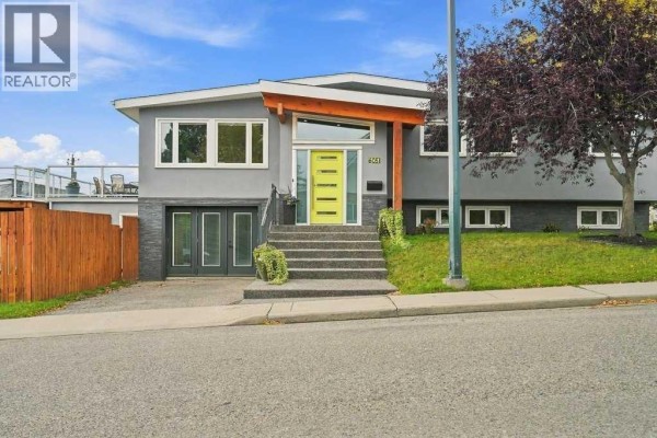 Modern house exterior with a grey stucco finish, wood accents, and a bright yellow door. - 6051 Dalgetty Drive Nw, Calgary