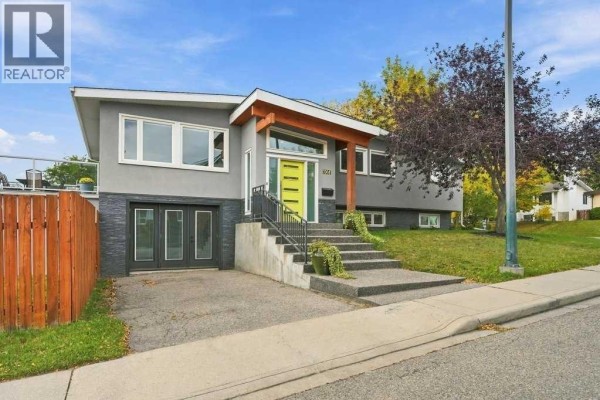 Front exterior of a modern house with a grey stucco finish and a prominent yellow door. - 6051 Dalgetty Drive Nw, Calgary