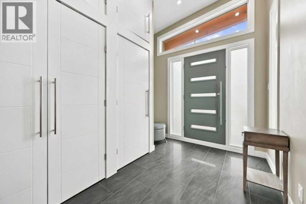 Foyer with white storage cabinets, a grey front door, and large floor tiles. - 6051 Dalgetty Drive Nw, Calgary