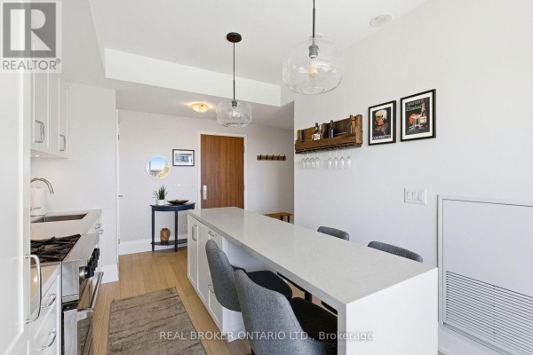 Kitchen island with grey stools and white cabinetry, with a wooden door in the background. - 606 - 25 Malcolm Road, Toronto