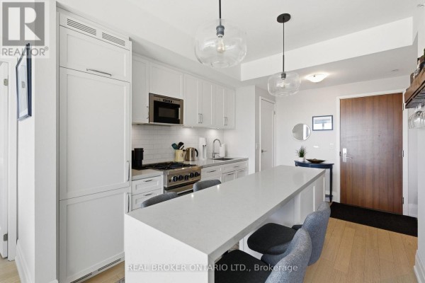 White kitchen with island, stainless steel appliances, and wooden entryway. - 606 - 25 Malcolm Road, Toronto