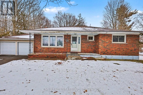 Front view of the red brick bungalow with a two-car garage and snow. - 606 Glen Miller Road, Quinte West