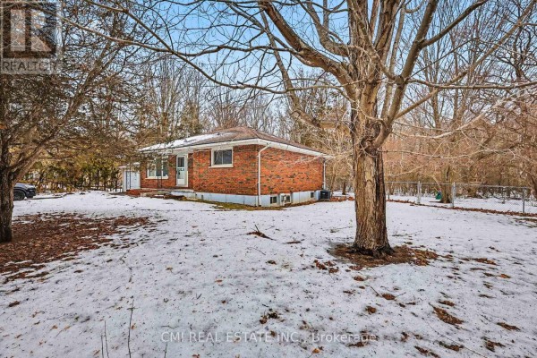 Side exterior view of the brick bungalow with trees and snow-covered ground. - 606 Glen Miller Road, Quinte West