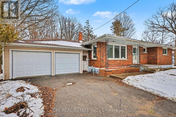 Side view of the bungalow showing the attached two-car garage and brick facade. - 606 Glen Miller Road, Quinte West