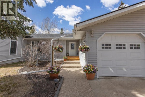 Close-up of the house entrance with a pathway, hanging flower baskets, and a double garage door. - 606 Pigeon Close, Pelican Point