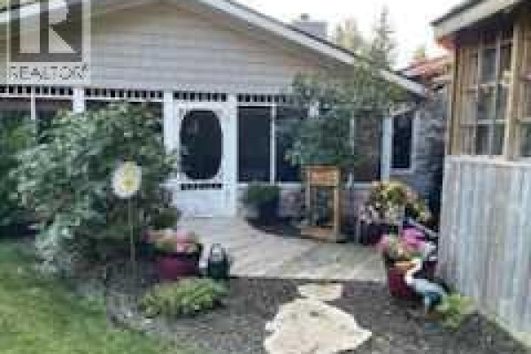 Front view of the house with a screened-in porch, deck, and surrounding garden elements. - 606 Pigeon Close, Pelican Point