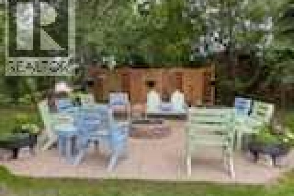 A patio area with colorful chairs, a fire pit, and a wooden structure in the background. - 606 Pigeon Close, Pelican Point