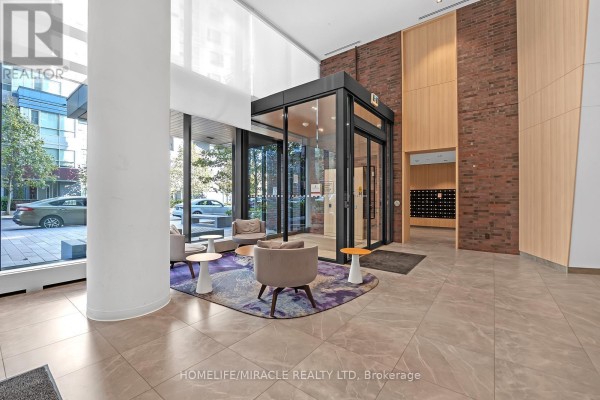 Apartment building lobby with seating area, large windows, marble floors, and brick accent wall. - 607 - 20 Tubman Avenue, Toronto