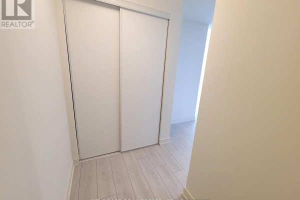 Hallway with white sliding closet doors and light wood-look flooring. - 607 - 8010 Derry Road, Milton