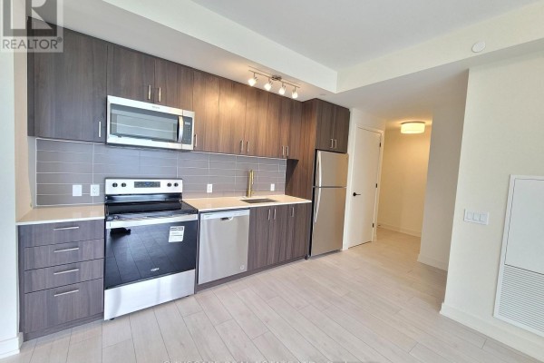 Apartment kitchen with dark wood cabinets, stainless steel appliances, and light grey backsplash. - 607 - 8010 Derry Road, Milton
