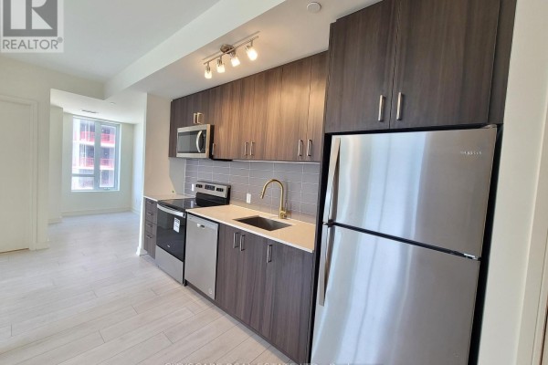Apartment kitchen with dark wood cabinets, stainless steel appliances, and view of living area. - 607 - 8010 Derry Road, Milton