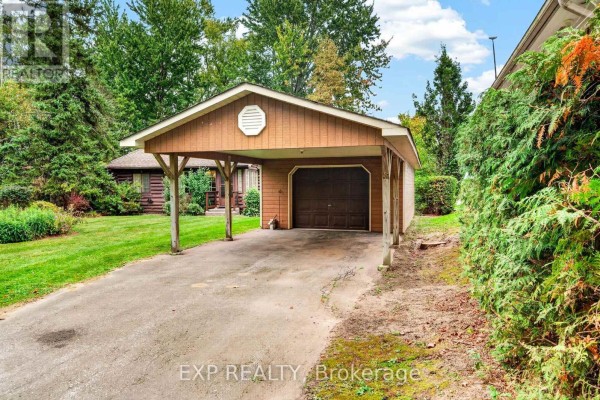 Driveway leading to the detached garage and carport, with dense green hedging on the right. - 607 Duclos Point Road, Georgina