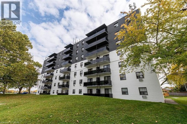 Exterior view of a multi-story apartment building with balconies and green lawn. - 607 Heritage Drive Unit# 306, Kitchener