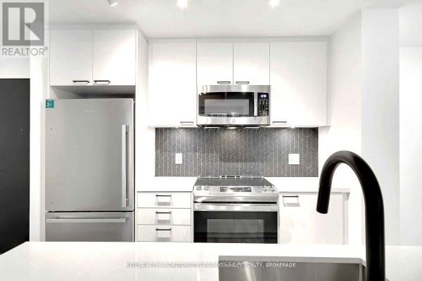 Kitchen with stainless steel refrigerator, microwave, and stove, featuring white cabinets and a gray herringbone backsplash. - 608 - 1808 St Clair Avenue W, Toronto