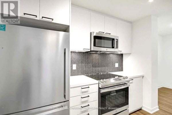 Close-up view of a modern kitchen with white cabinetry, stainless steel appliances, and a gray tiled backsplash. - 608 - 1808 St Clair Avenue W, Toronto