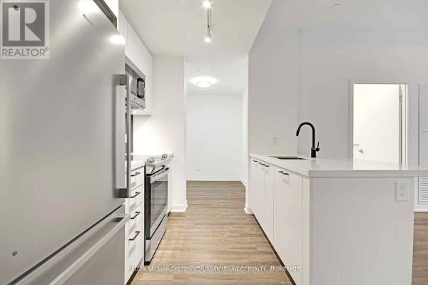 View of a galley-style kitchen with white cabinets, stainless steel appliances, and a black faucet on a quartz countertop. - 608 - 1808 St Clair Avenue W, Toronto