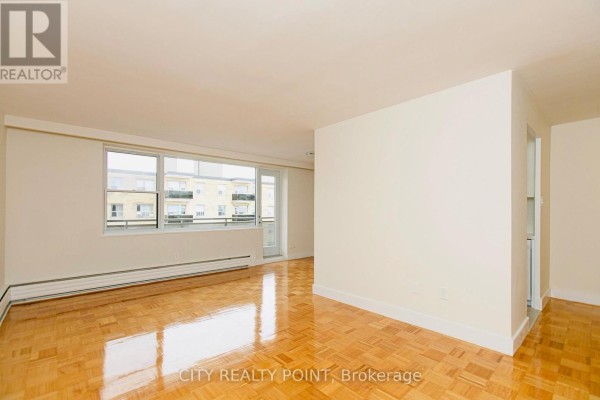 Living room with a large window showing an exterior view of a building and balcony. - 608 - 2 Grandstand Place, Toronto