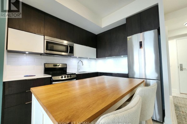 Corner kitchen with dark wood and white cabinets, stainless steel appliances, and island. - 608 - 56 Annie Craig Drive, Toronto