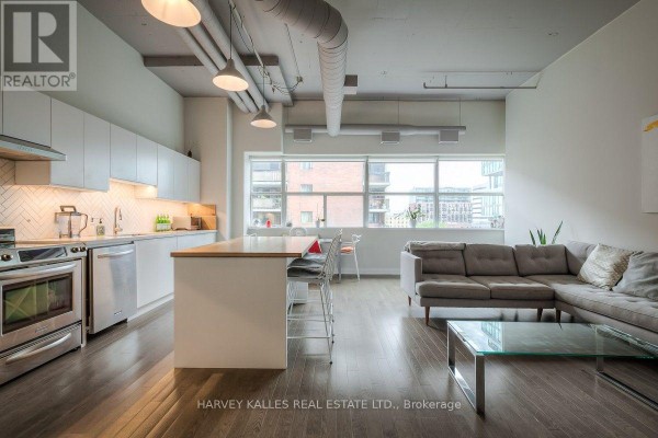 Open concept living area with a grey sectional sofa, glass coffee table, and large window view. - 608 - 700 King Street W, Toronto
