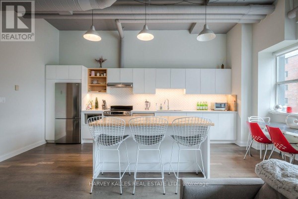 Kitchen island with white wire stools facing a modern white kitchen with a stainless steel refrigerator. - 608 - 700 King Street W, Toronto