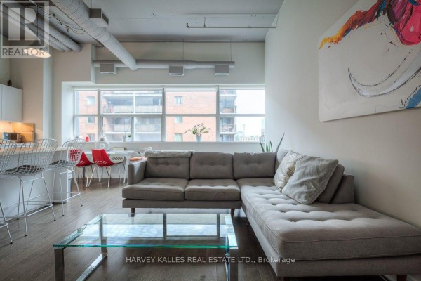 Living room with a large grey sectional sofa, glass coffee table, and abstract art on the wall. - 608 - 700 King Street W, Toronto