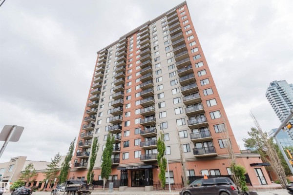 Low-angle view of The Legacy apartment building's brick and glass facade against a cloudy sky. - #608 10303 105 St Nw, Edmonton