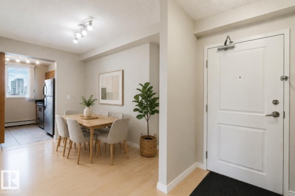 Apartment entryway with a white door and a dining area with a table, chairs, and kitchen view. - #608 10303 105 St Nw, Edmonton