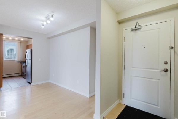 Apartment entryway with a white door and an open-concept living and dining area with a kitchen view. - #608 10303 105 St Nw, Edmonton