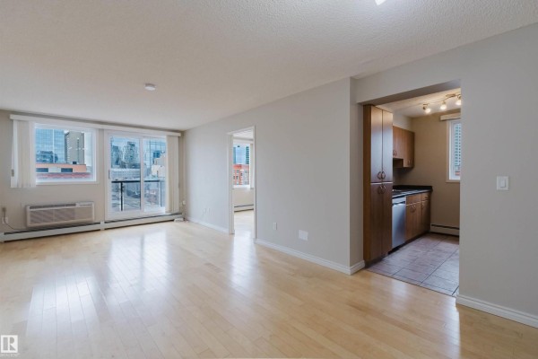 Apartment living room with light wood floors, large windows, balcony access, and an open kitchen view. - #608 10303 105 St Nw, Edmonton