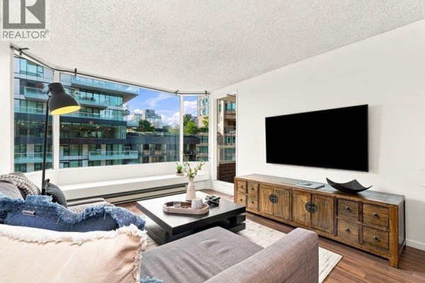 Living room featuring a sectional sofa, large bay window, and a wooden media console. - 608 1330 Hornby Street, Vancouver