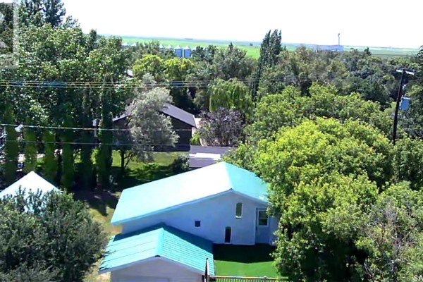 Exterior view of a light-colored house with a garage, wooden deck, and snowy yard. - 608 Whyte Street, Loreburn