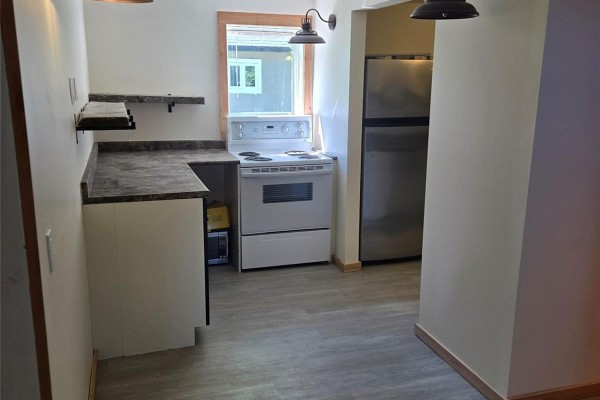 Kitchen area with white cabinets, subway tile backsplash, sink, and a staircase leading up. - 608 Whyte Street, Loreburn