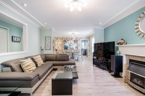 Living room with a grey sectional sofa, fireplace with marble surround, and light wood flooring. - 6081 W Boundary Drive, Surrey