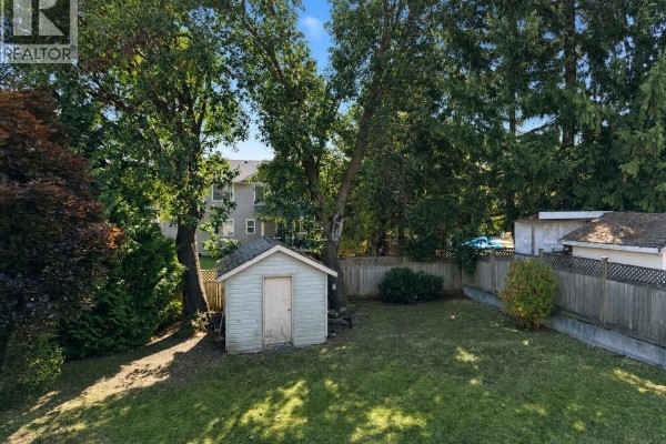 Backyard with a green lawn, mature trees, a small wooden shed, and a wooden fence. - 6083 Sierra Way, Nanaimo