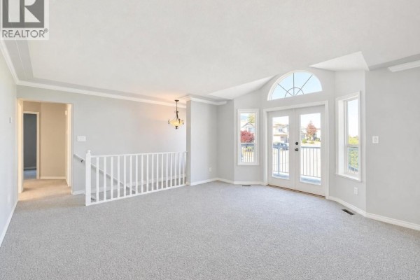 Spacious living room with grey carpet, white trim, a vaulted ceiling, and a glass-doored balcony. - 6083 Sierra Way, Nanaimo
