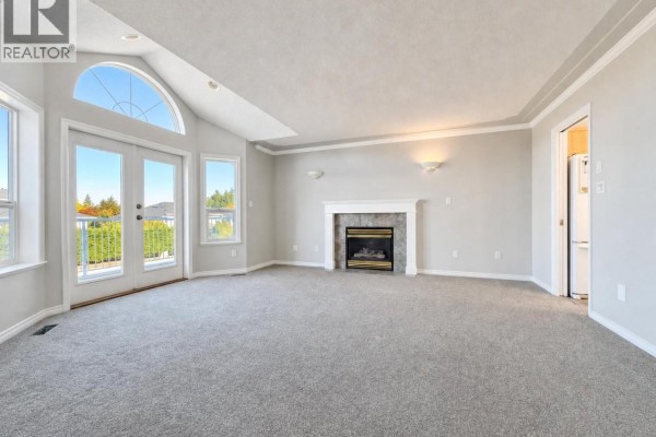 Living room with grey carpet, a gas fireplace with a white mantle, and large windows. - 6083 Sierra Way, Nanaimo