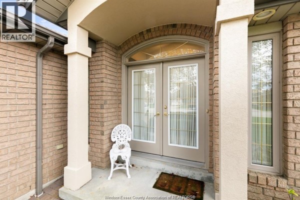 Close-up of the double glass entry doors with decorative panels and a white metal chair. - 6085 Natalie Court, Lasalle