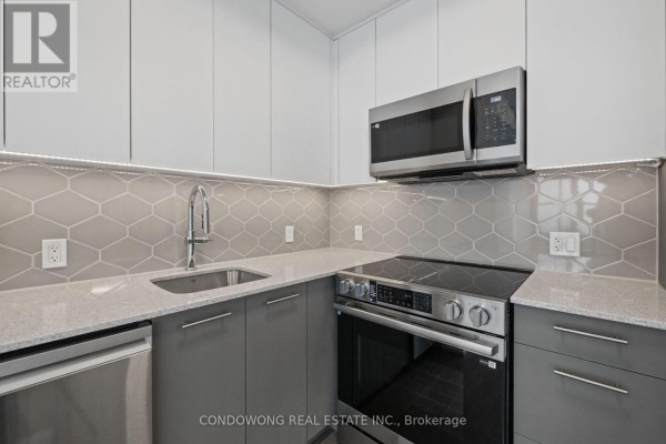 Close-up of a modern kitchen with grey cabinets, a stainless steel sink, stove, and microwave. - 609 - 30 Francis Street S, Kitchener