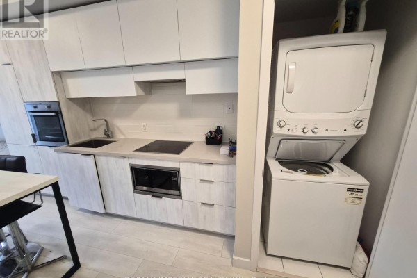 Kitchenette with white cabinets, integrated appliances, and a stacked washer and dryer unit. - 609 - 8 Eglington Avenue E, Toronto