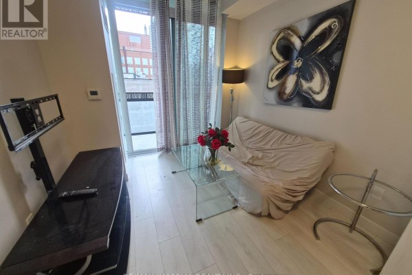 Living area with a glass coffee table, sofa covered in a throw, a floor lamp, and abstract wall art. - 609 - 8 Eglington Avenue E, Toronto