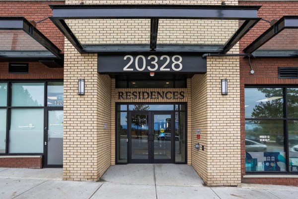 Entrance to "20328 RESIDENCES" with double glass doors and brick facade. - 609 20328 86 Avenue, Langley