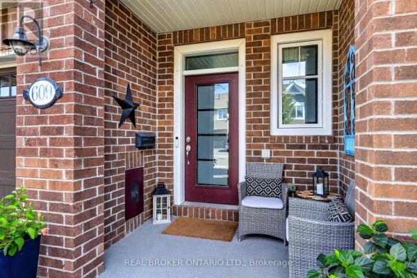 Close-up of the brick townhouse entrance with a red door, glass panels, and seating on the porch. - 609 Egret Way, Ottawa