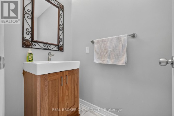 Powder room with a white sink, wooden vanity, and a decorative mirror on a light grey wall. - 609 Egret Way, Ottawa