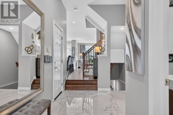 Interior hallway with a staircase, wood flooring, white doors, and a large mirror reflecting the entryway. - 609 Egret Way, Ottawa