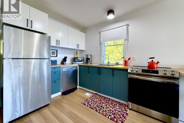Modern kitchen with stainless steel refrigerator, teal cabinets, wood countertops, and silver appliances. - 609 Glen Road, Gibsons