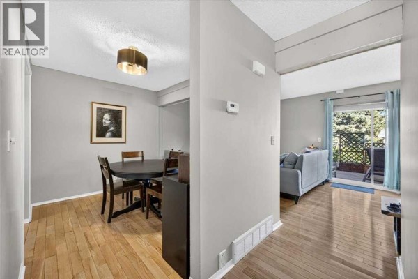 Dining area with a round table and chairs, adjacent to a hallway leading to the living room. - 61, 4940 39 Avenue Sw, Calgary