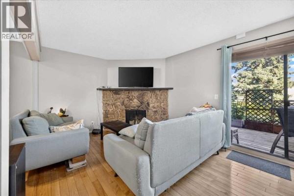 Living room with two sofas, a stone fireplace, and a sliding glass door opening to a deck. - 61, 4940 39 Avenue Sw, Calgary