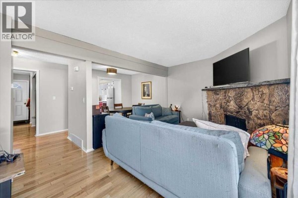 Living room with sofas, a stone fireplace, and a view into the dining area and entryway. - 61, 4940 39 Avenue Sw, Calgary
